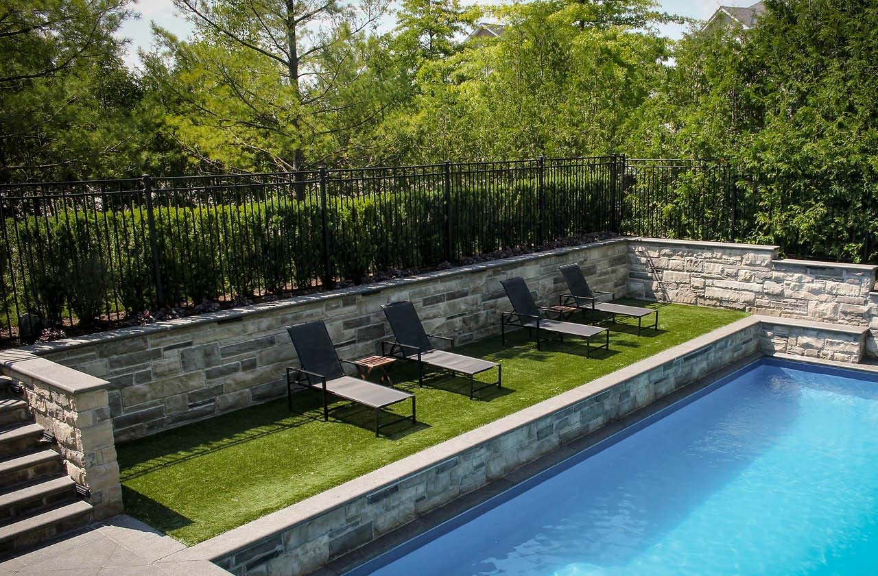 A picture perfect pool side seating area surrounded by stunning stonework and a Nuvo Iron fence.