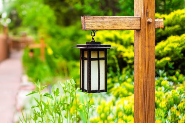 Japan hanging lantern lamp light on wooden post in Japanese garden with path by house temple and green foliage background