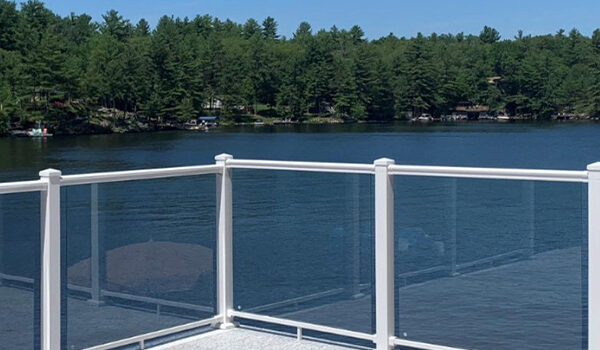 A white metal deck railing with glass panels overlooking a lake.