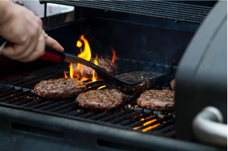 A person grills burgers over a flame.