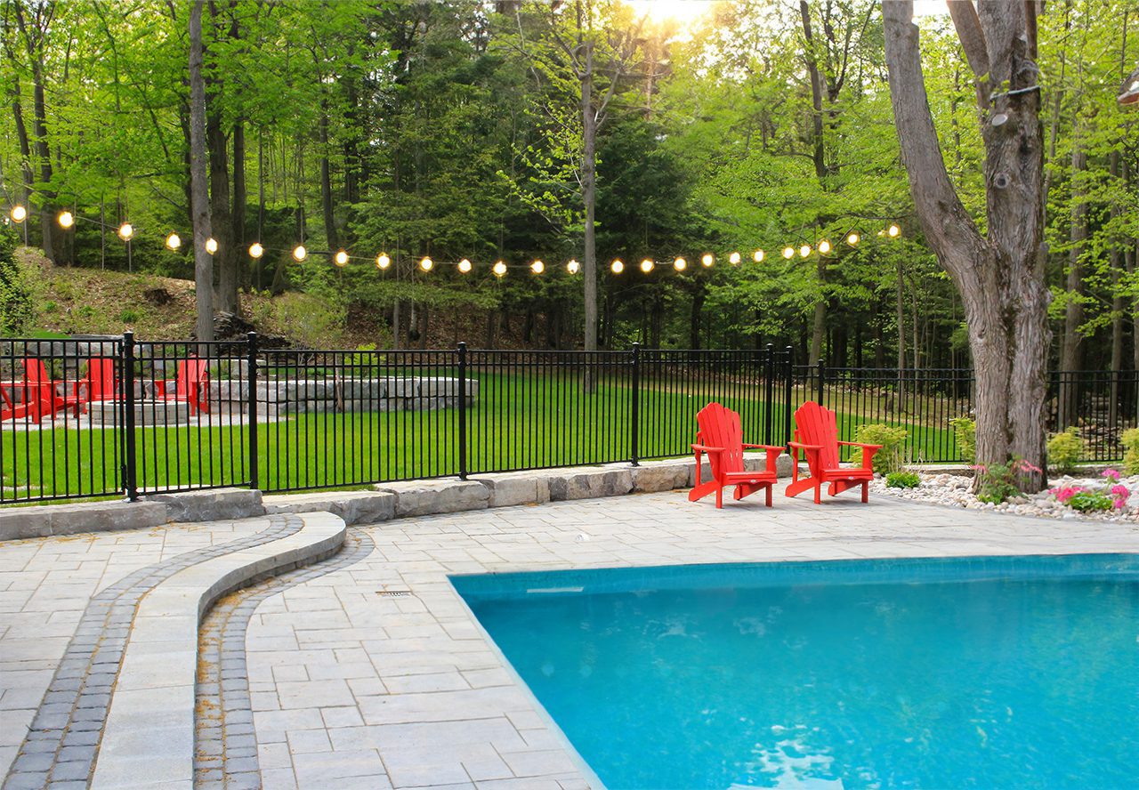 Black iron fence and railing around a backyard pool at dusk with string lights