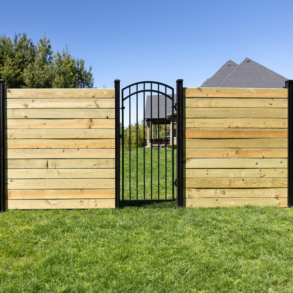 Nuvo Iron black arched iron gate installed in a horizontal wood privacy fence