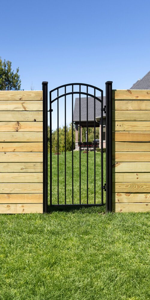 Nuvo Iron black arched iron gate installed in a horizontal wood privacy fence