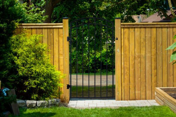 Pre-welded black iron gate with arched top and vertical bars installed in a wood fence line