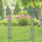 Gray chain-link fence with a matching walk-through gate installed in a backyard, surrounded by a willow tree, evergreen shrubs, and blooming pink flowers on a green lawn.