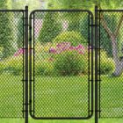 Black chain link gate installed in a lush backyard setting with green trees, shrubs, and pink flowering plants in the background.