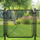 Black chain link gate installed in a lush backyard setting with a tree, evergreen shrubs, and pink flowering plants in the background
