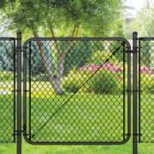 Black chain link gate installed in a lush backyard setting with a tree, evergreen shrubs, and pink flowering plants in the background