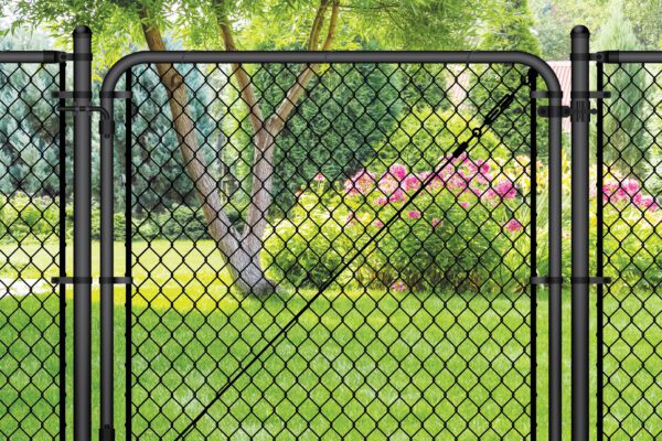 Black chain link gate installed in a lush backyard setting with a tree, evergreen shrubs, and pink flowering plants in the background