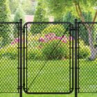 Black chain link gate installed in a green backyard setting with a tree, evergreen shrubs, and pink flowering plants in the background.