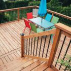 Wood deck with black round balusters and outdoor patio furniture including red, blue, and green chairs around a table with umbrella