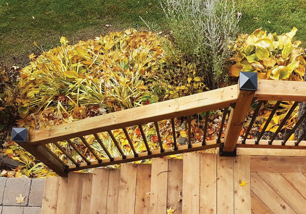 Black pyramid-style Nuvo Iron post cap installed on a wood deck railing post.