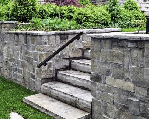 nuvo iron outdoor stair handrail black metal deck accessory mounted on stone steps with landscaped garden retaining wall